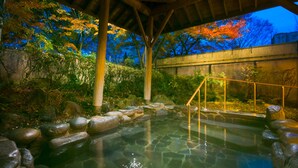 Un onsen japonés tradicional con estructura de madera, tina de piedra y follaje circundante.