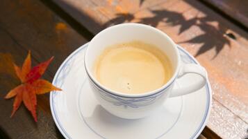 A white cup with blue patterns on a saucer, placed on a wooden surface with a red maple leaf beside it.
