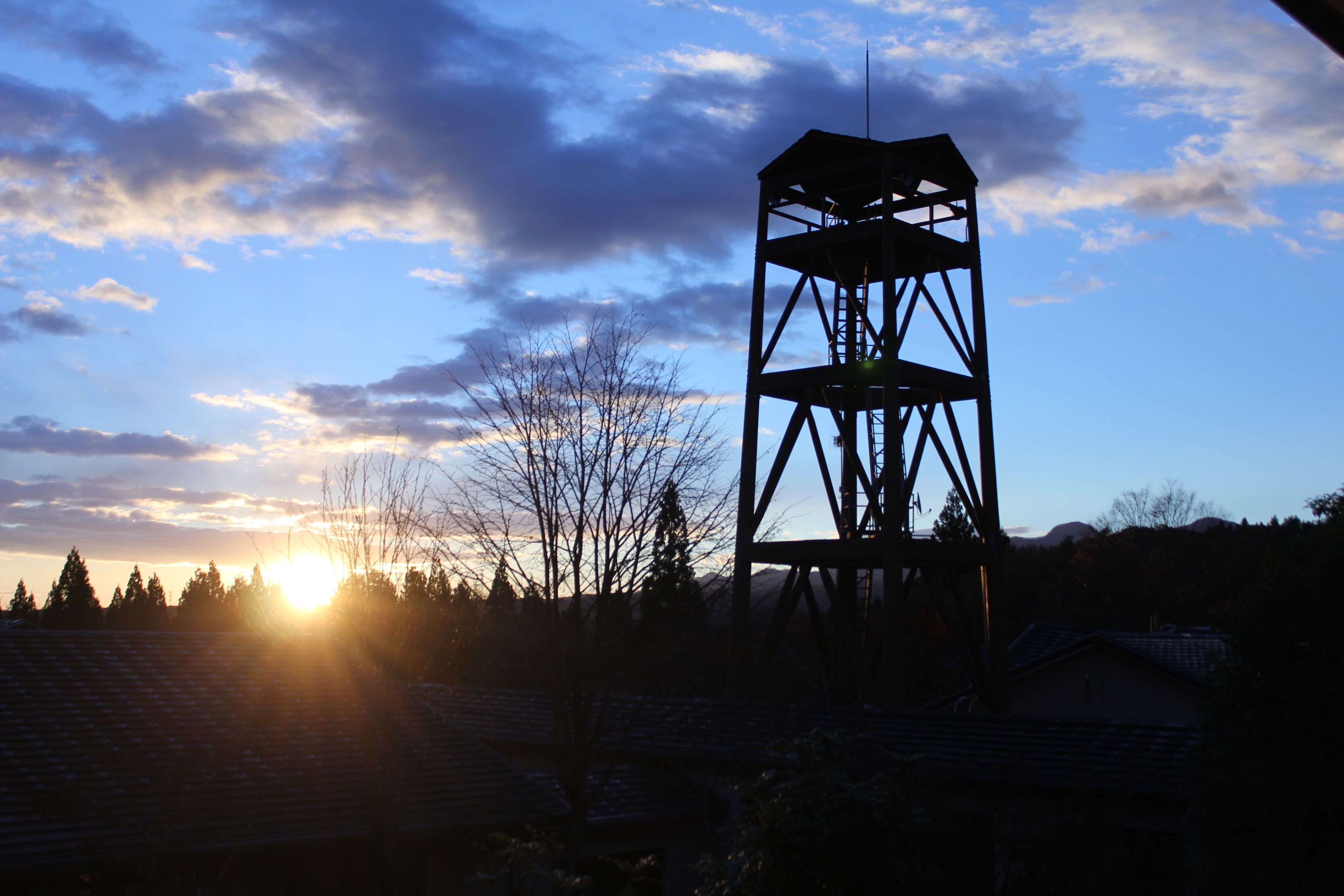 A tall metal structure with a triangular roof, set against a backdrop of a sunset and a clear sky.
