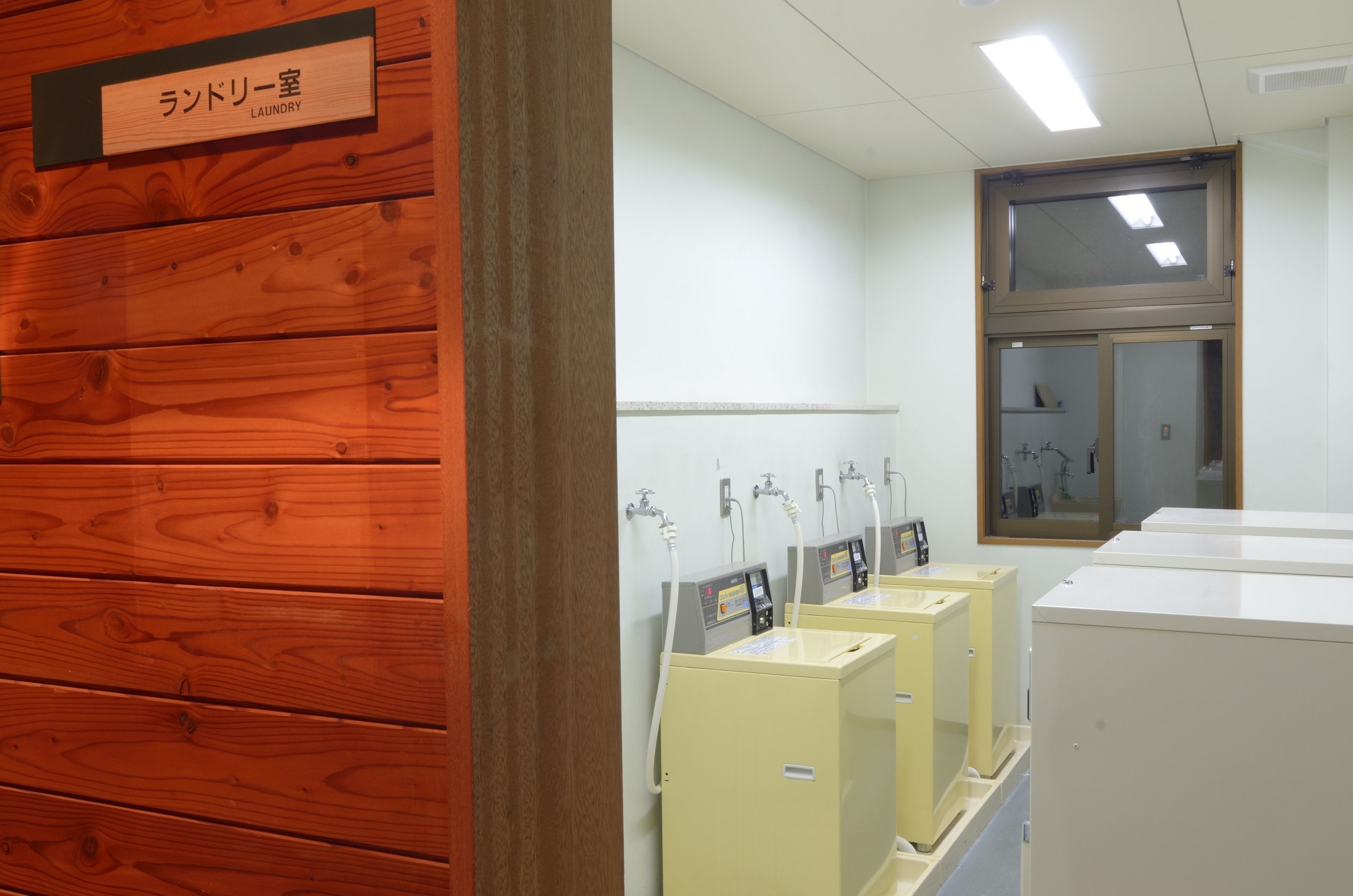 A laundry room with wooden paneling and a sign indicating it is the laundry area. There are multiple washing machines and dryers lined up against the wall.