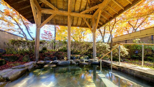 Un jardín japonés tradicional con un estanque sereno, estructuras de madera y follaje otoñal.