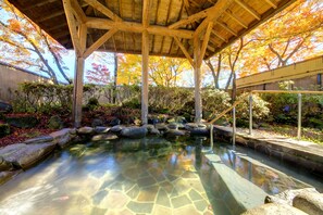 Un jardín japonés tradicional con un estanque sereno, estructuras de madera y follaje otoñal.