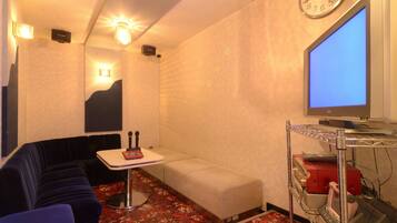A hotel room with a sofa, a small table, a television, and a wall clock.