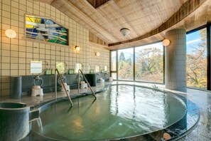 Una amplia piscina interior con techo de madera y vistas a árboles otoñales.