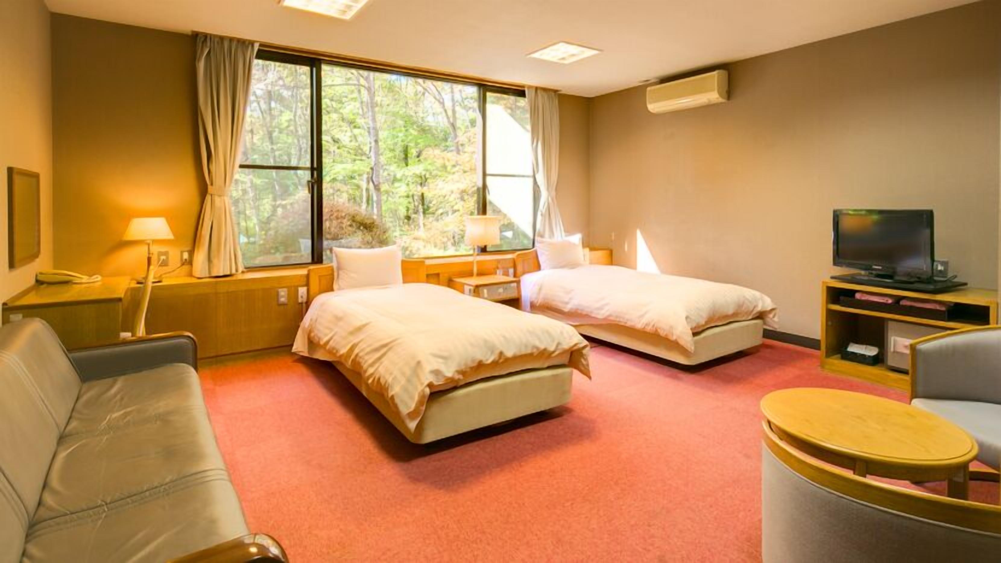 A hotel room with two beds, a sofa, a TV, and a window with a view of trees.