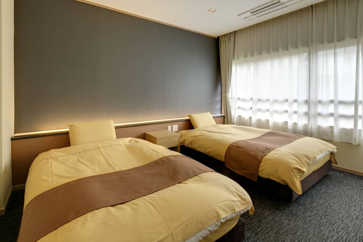 Een hotelkamer met twee bedden, een groot raam met dunne gordijnen en een neutraal kleurenpalet.
