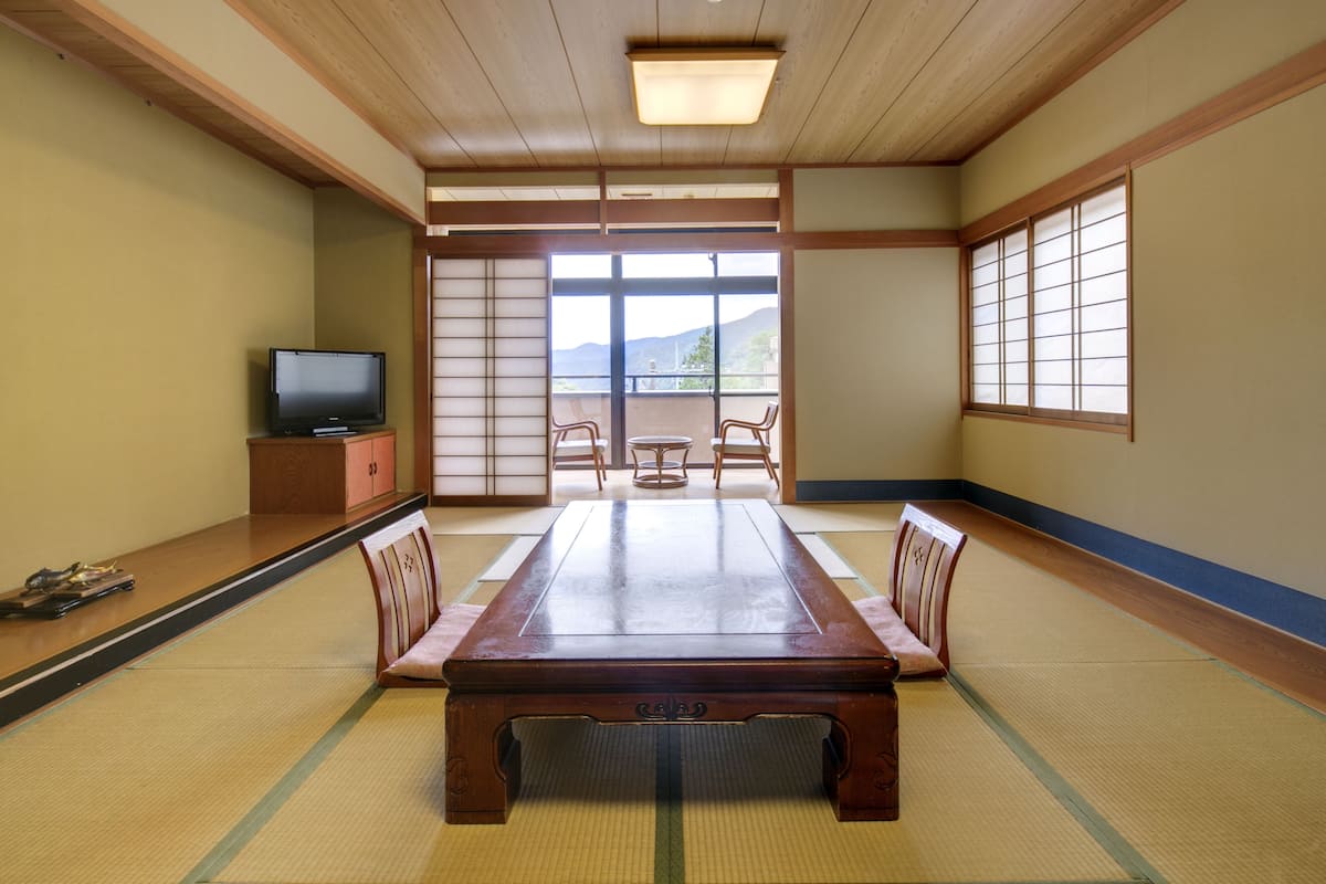 Een traditionele Japanse kamer met tatami vloerbedekking, een lage houten tafel en schuifdeuren die uitkomen op een balkon met uitzicht op bergen.