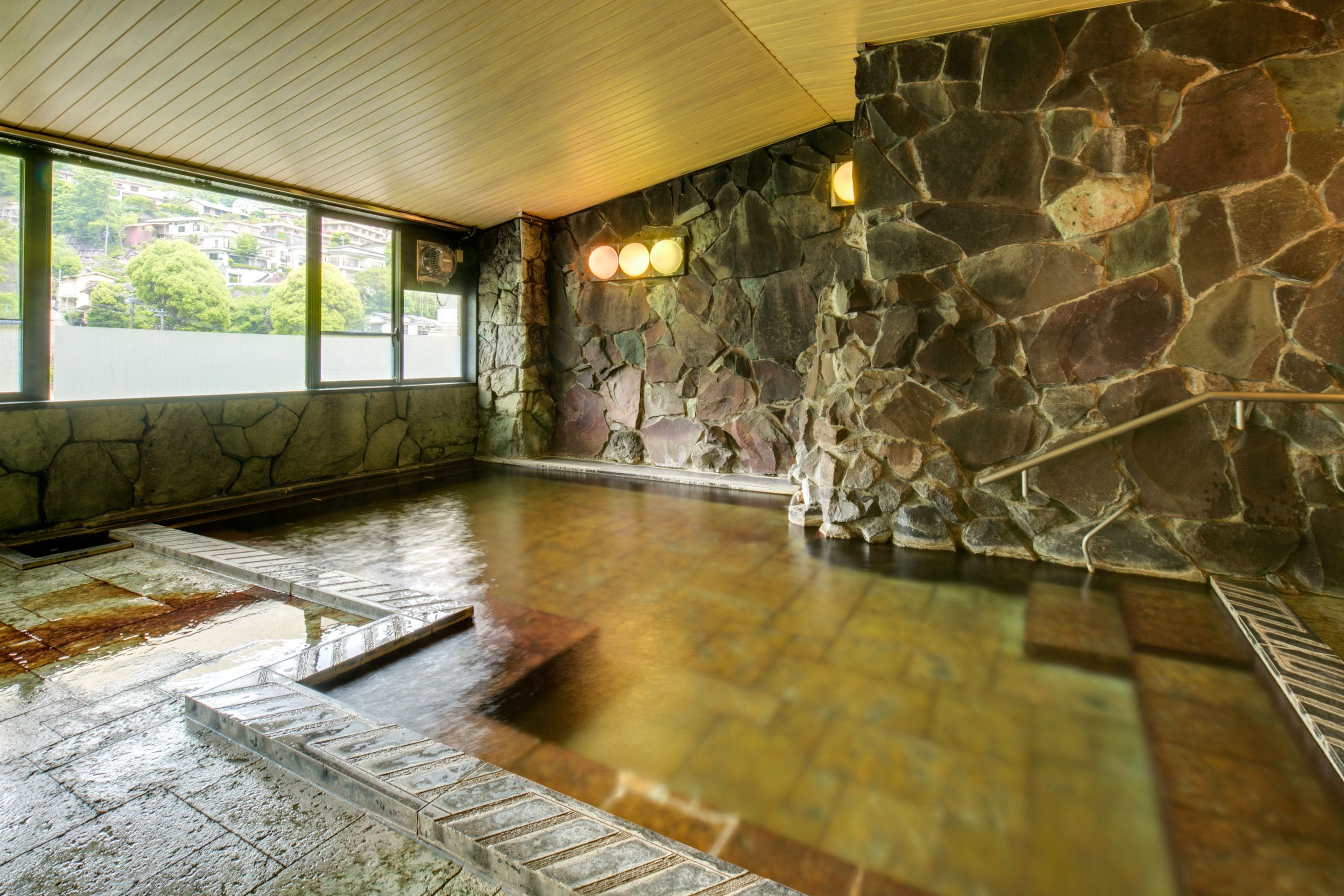 Una piscina interior con paredes de piedra, techo de madera y vistas a edificios exteriores.