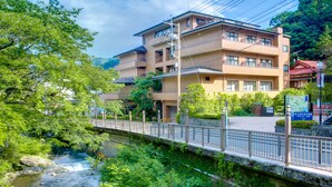 A multi-story building with balconies, a bridge, and a river. - Yugawara Mizunokaori (Yugawara)