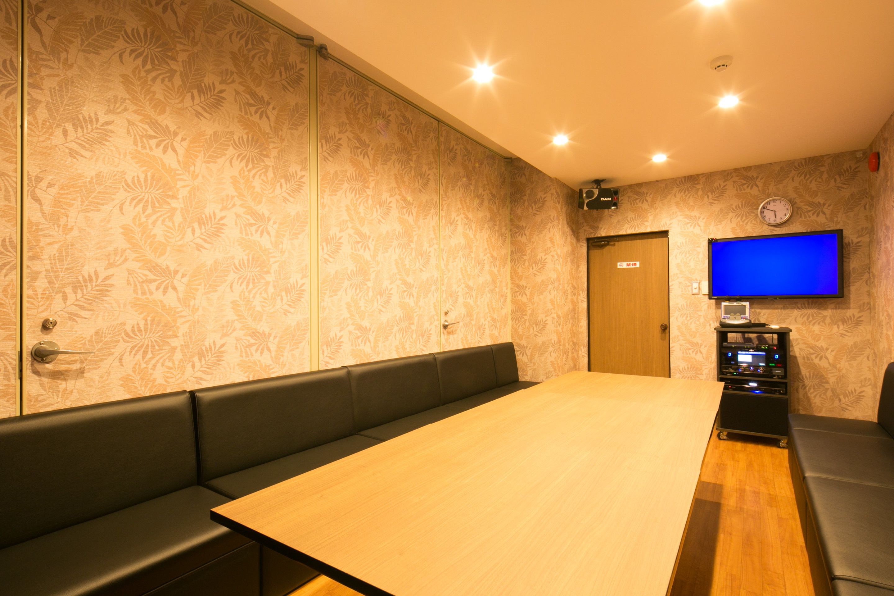 Een vergaderruimte met een lange tafel, zwarte gestoffeerde zitplaatsen, een flatscreen televisie en een klok aan de muur.