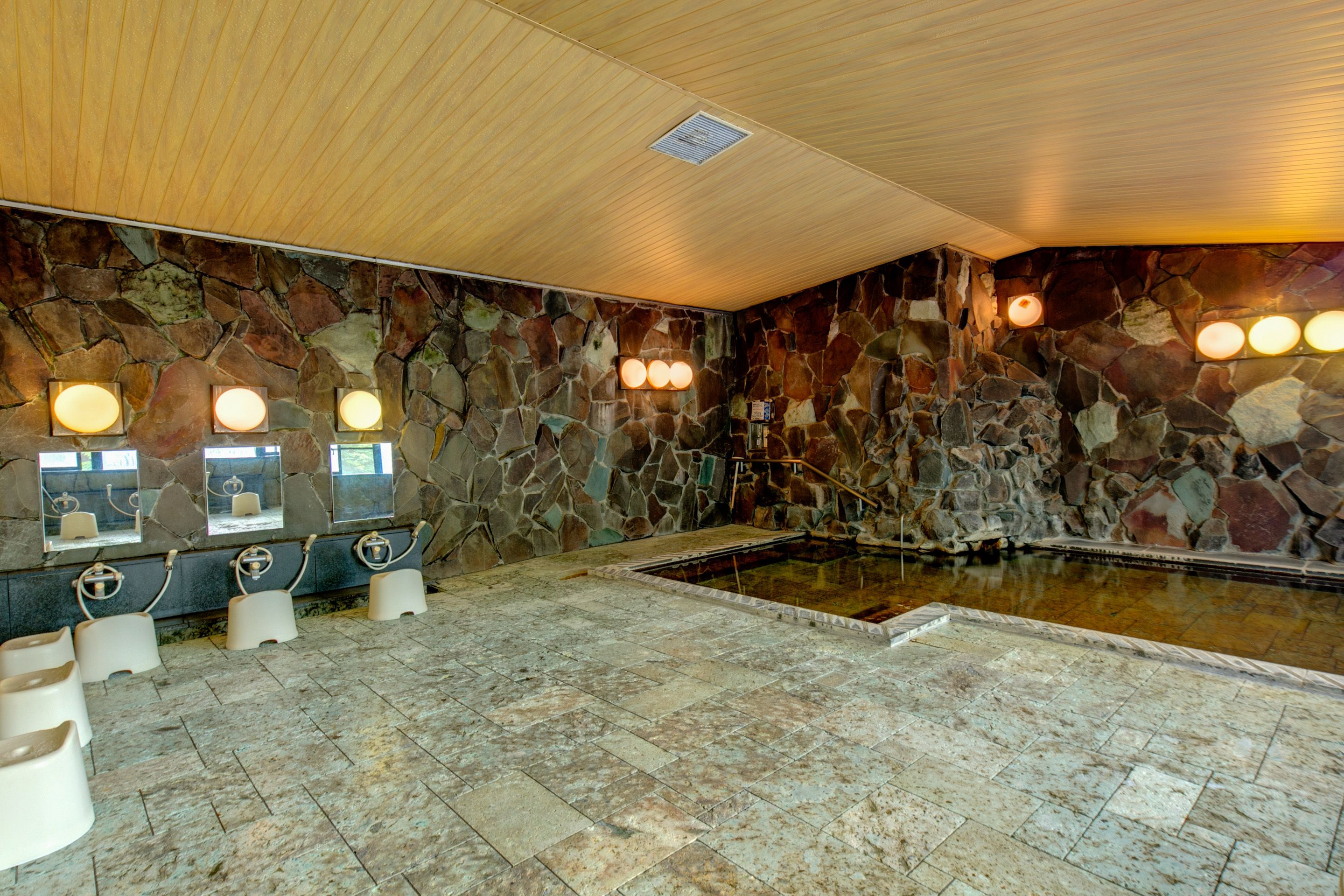 A stone-walled indoor pool area with multiple benches and a central pool.