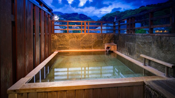 A traditional wooden bath with a stone wall, wooden railings, and a view of mountains. - Yugawara Mizunokaori (Yugawara)