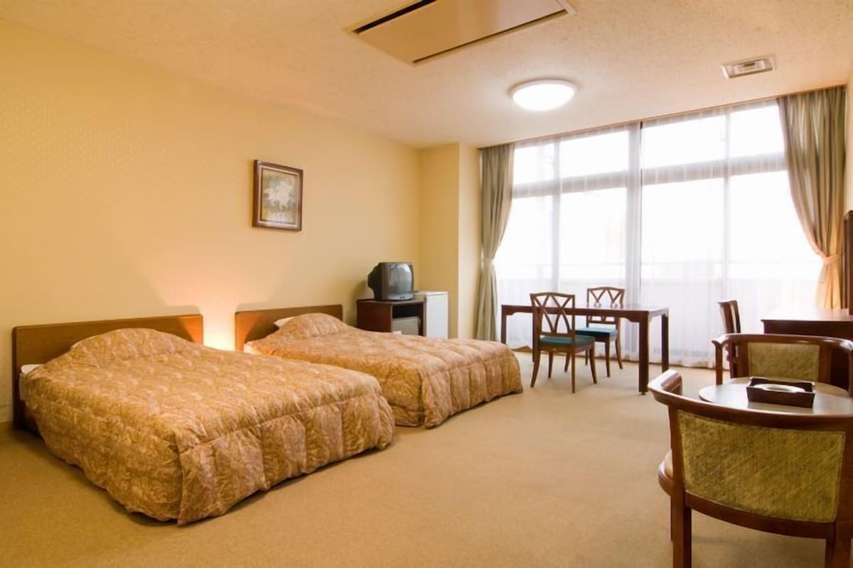 Een hotelkamer met twee bedden, een bureau, een stoel en een televisie.
