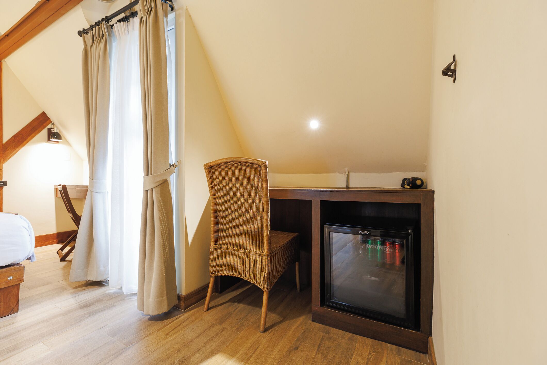 Een slaapkamer met een bed, een rieten stoel, een klein bureau met een computer en een minibar.