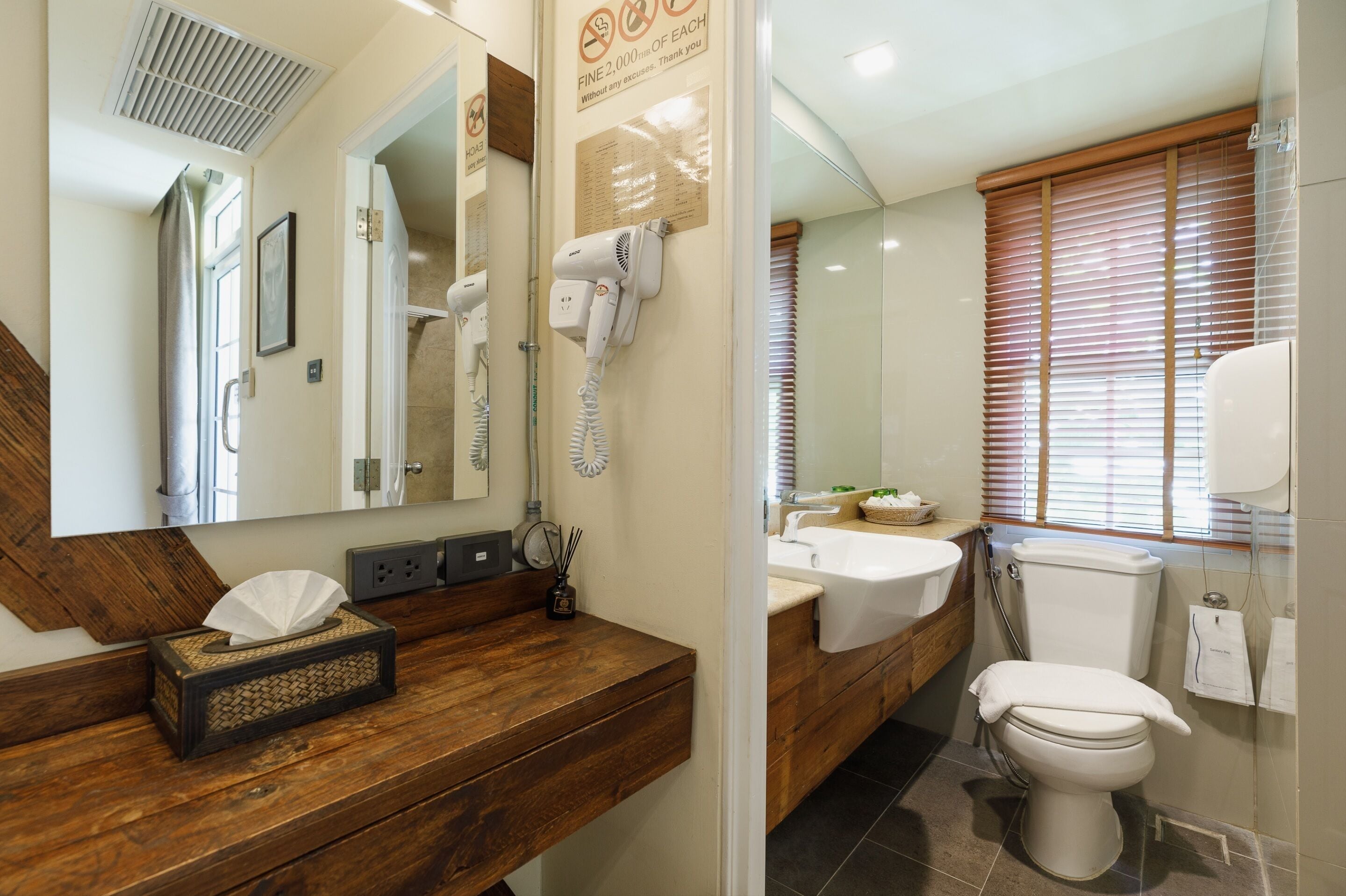 A bathroom with a wooden vanity, a mirror, a hairdryer, a sink, and a toilet.