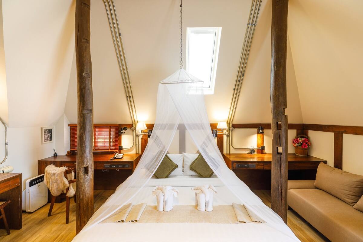 A bedroom with a canopy bed, wooden furniture, bedside tables with lamps, and a window.