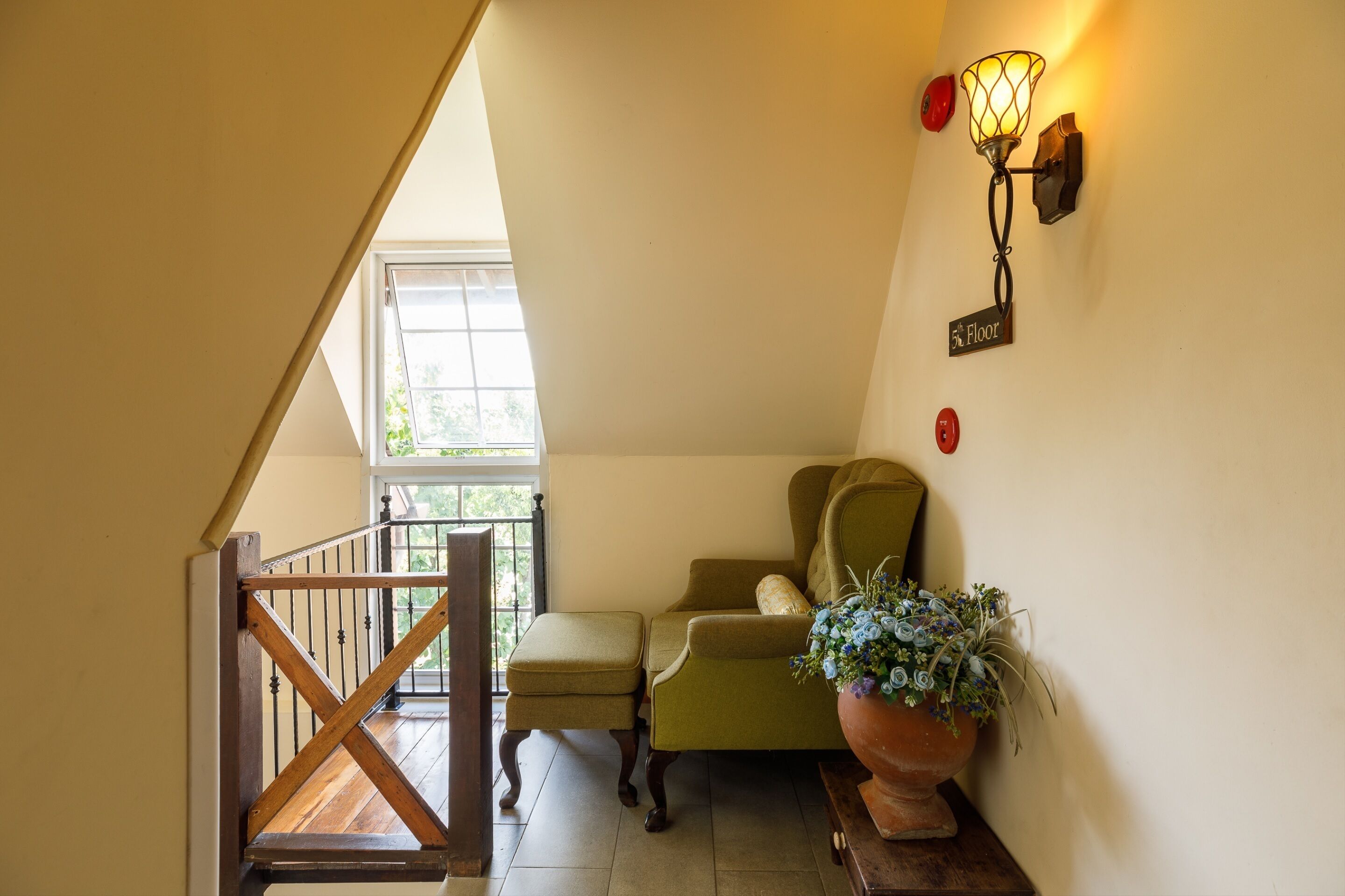A staircase with a wooden railing, a green armchair, a potted plant, and a wall-mounted light fixture.