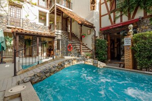 Zona de piscina con un puente de piedra, un flotador salvavidas y un cartel para LE Charcoa Hotel.