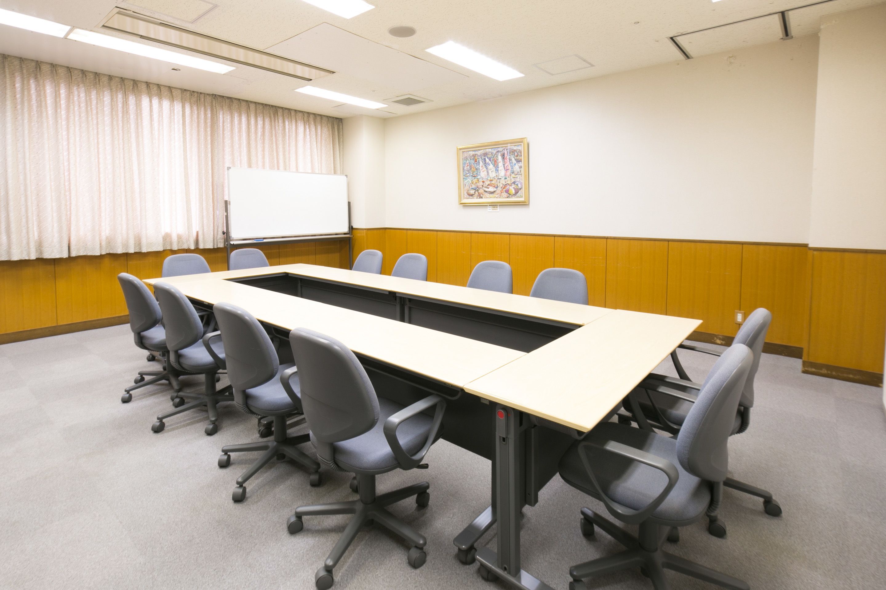 A conference room with a long table, six chairs, a whiteboard, and a painting on the wall.