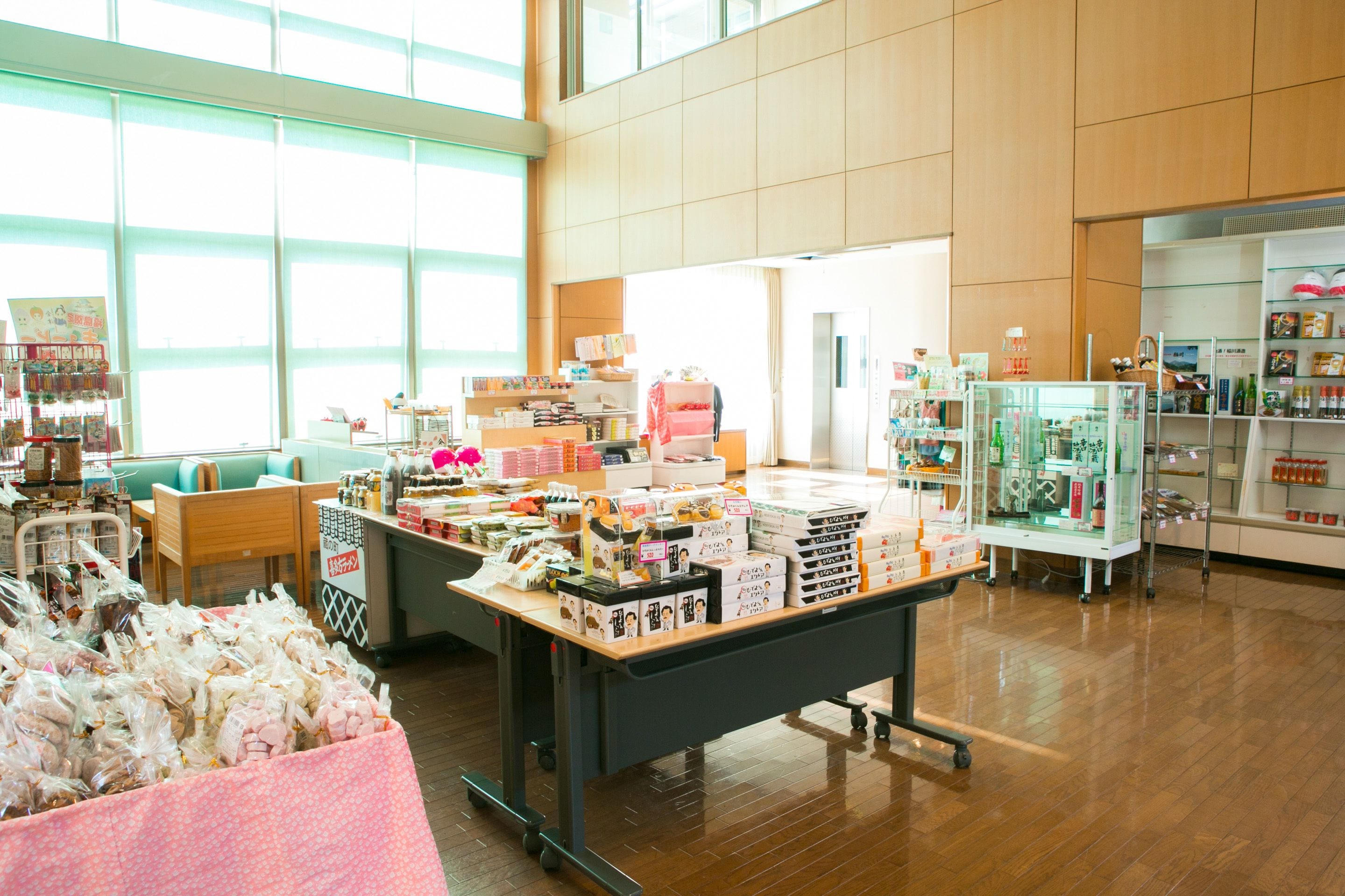 A spacious indoor area with a wooden floor, a central display table with various items, and a seating area with green chairs.