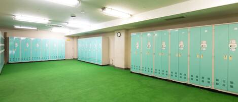 A locker room with green lockers, a clock on the wall, and a green carpeted floor.