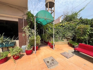 A reception area with a sign, potted plants, a red bench, and a water tank. - Hilltop Hotel (Karachi)