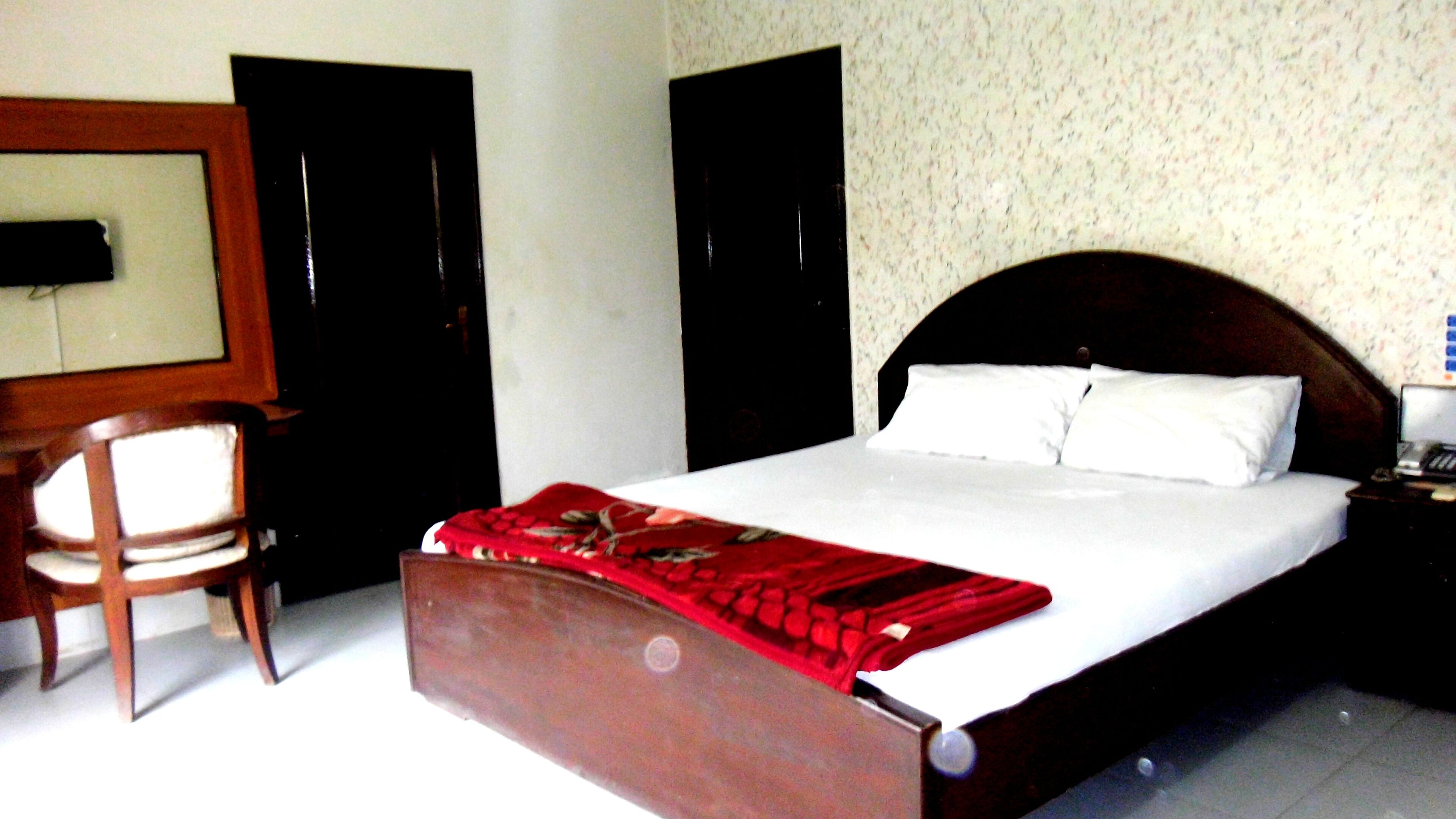 A hotel room with a bed, a chair, a desk, and a wall-mounted TV.