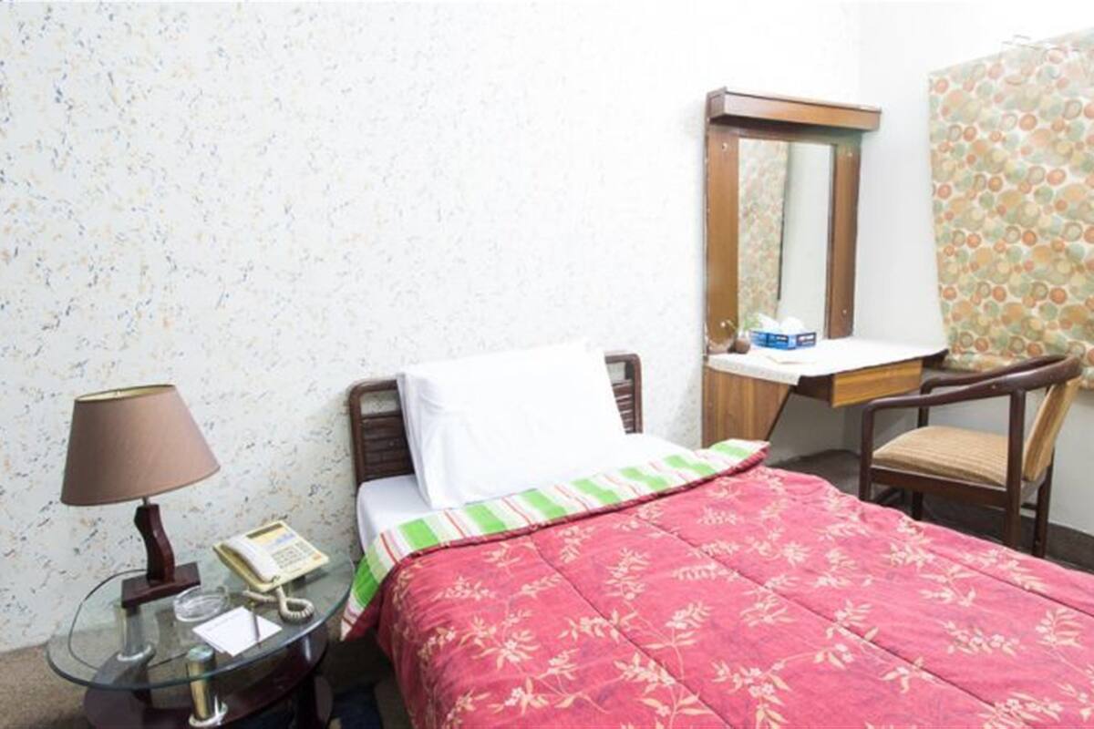 Una habitación pequeña y sencilla con cama, una silla, un escritorio y una lámpara.