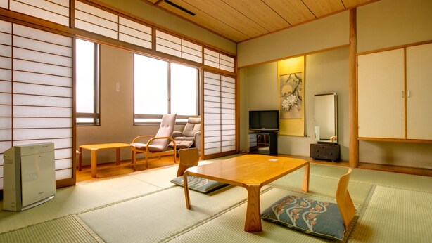 A traditional Japanese room with tatami flooring, a low wooden table, a cushioned bench, a television, and sliding doors. - Akoya Kaikan (Yamagata)