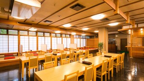 A spacious room with multiple wooden tables and chairs, large windows with blinds, and a wooden floor. - Akoya Kaikan (Yamagata)