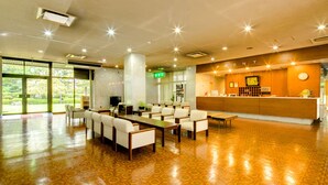 A spacious lobby with a reception desk, seating area, and large windows offering a view of greenery. - Akoya Kaikan (Yamagata)