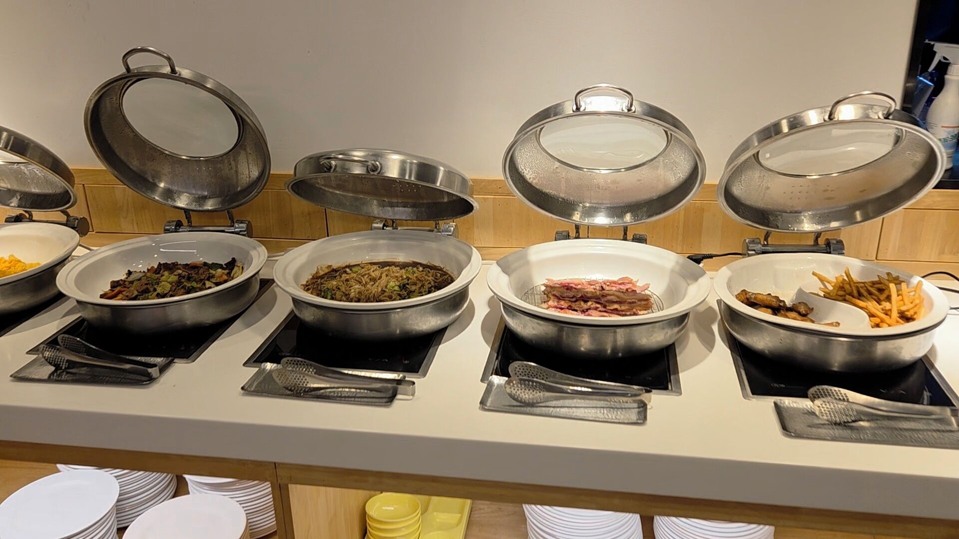 A buffet line with various dishes in metal bowls and pots, some with lids.