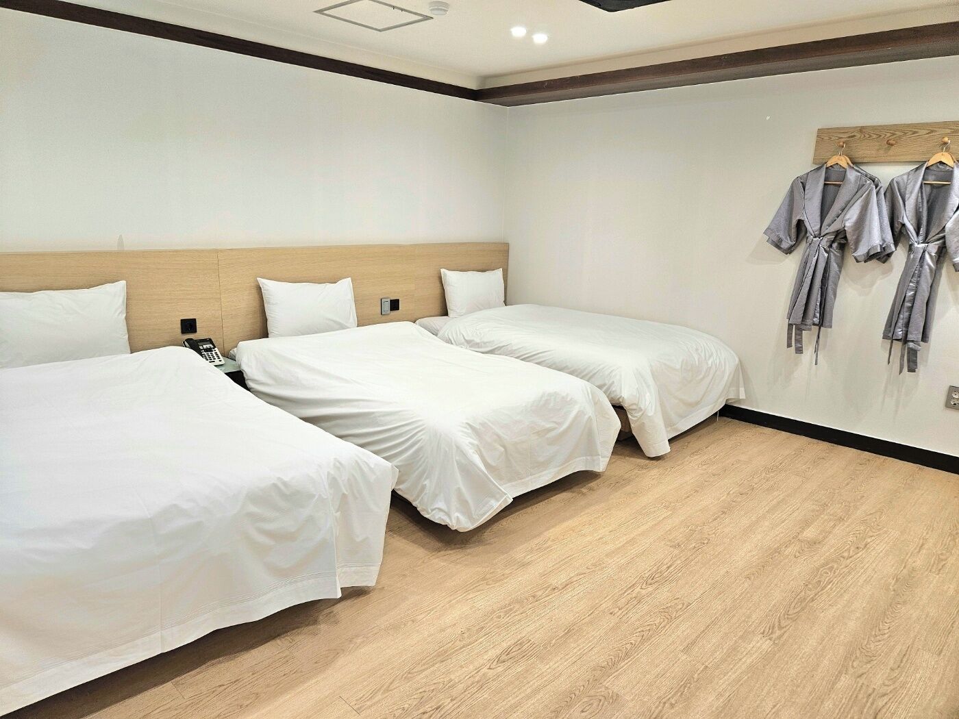A hotel room with two single beds, a wooden headboard, a wooden floor, and a wall-mounted robe rack.