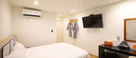 A hotel room with a bed, a desk with a computer, a TV, and a mirror.
