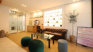 A modern hotel lobby with a glass coffee table, leather sofa, and green ottomans. - JB Plus Hotel (Busan)