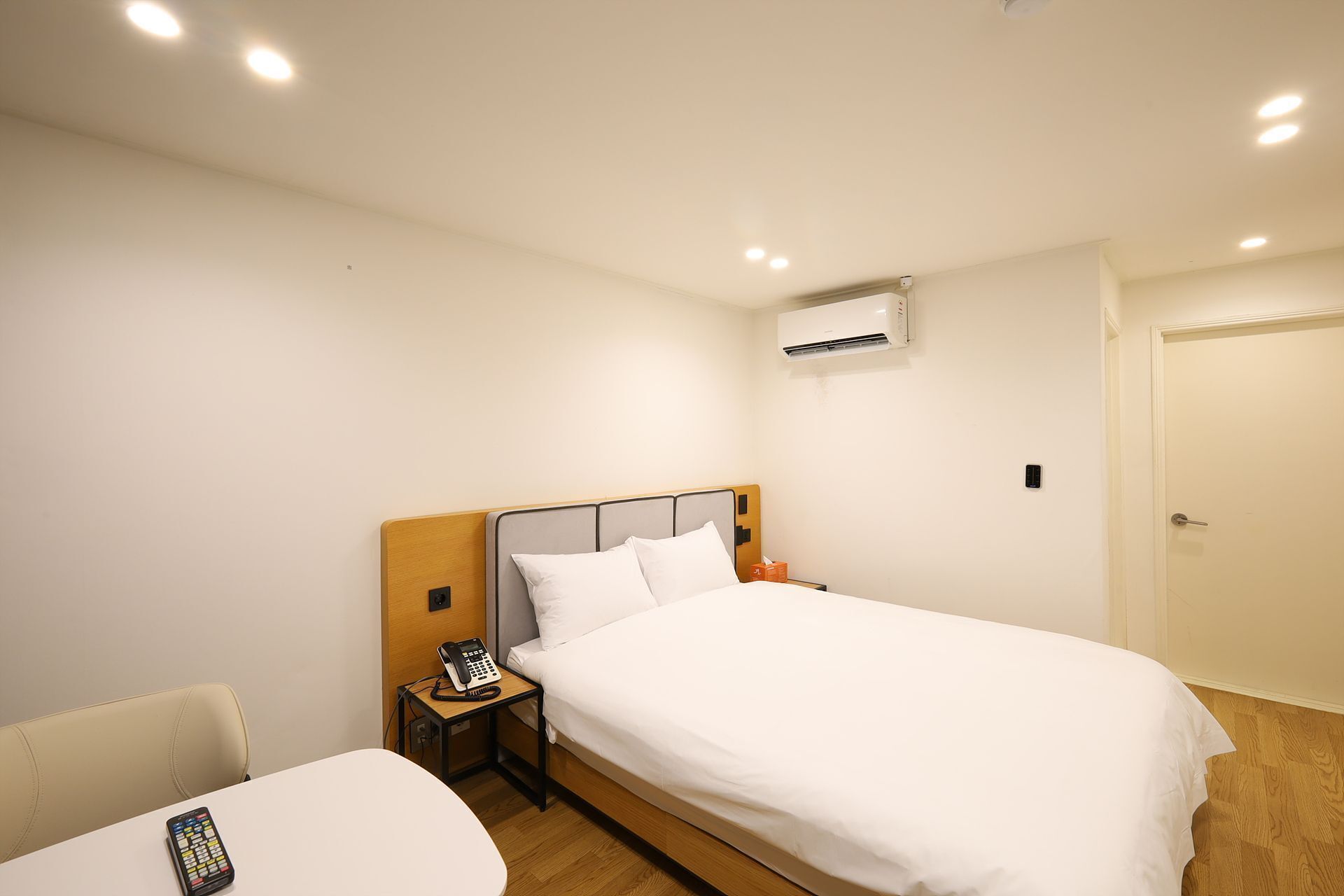 Habitación de hotel con cama, mesita de noche con teléfono, unidad de aire acondicionado y puerta.