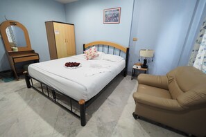 A bedroom with a bed, a wooden wardrobe, a mirror, a nightstand, a lamp, and a beige armchair. - Luxury Hotel (Kanchanaburi)