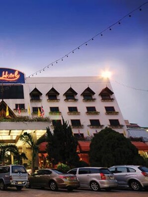 Un hotel con una fila de balcones, un cartel y un estacionamiento lleno de coches.