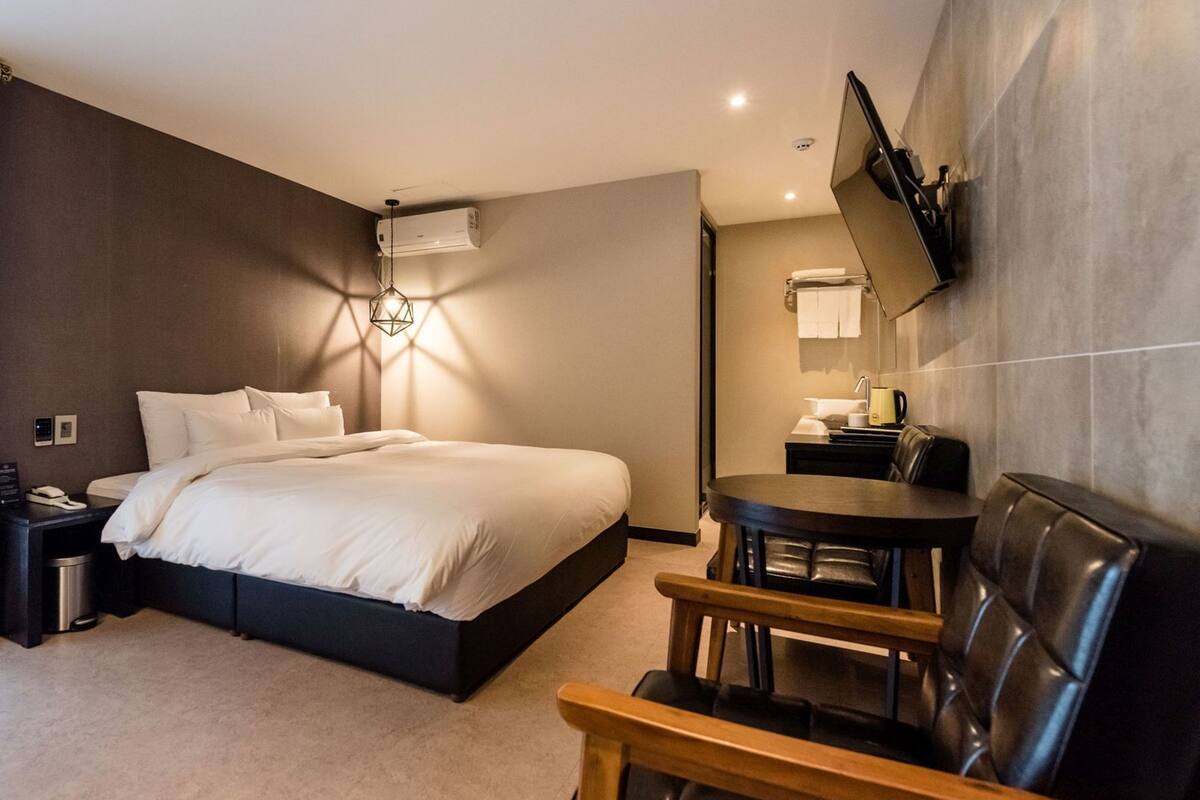 Une chambre d’hôtel moderne équipée d’un lit, d’une table de chevet, d’une lampe, d’une télévision et d’une petite table ronde avec des chaises.