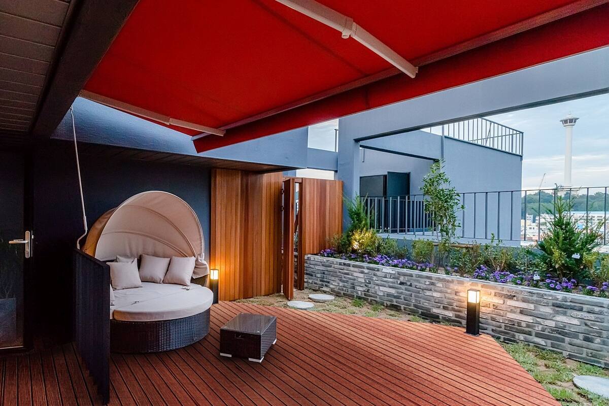 Un espace extérieur moderne, aménagé avec un banc circulaire rembourré, une petite table et un auvent rouge.
