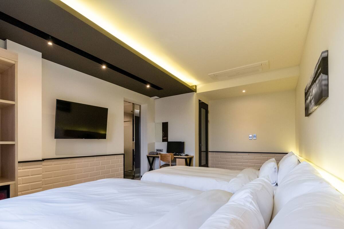 Une chambre d’hôtel avec un grand lit, un bureau avec un ordinateur, un téléviseur fixé au mur et une porte donnant sur une autre pièce.