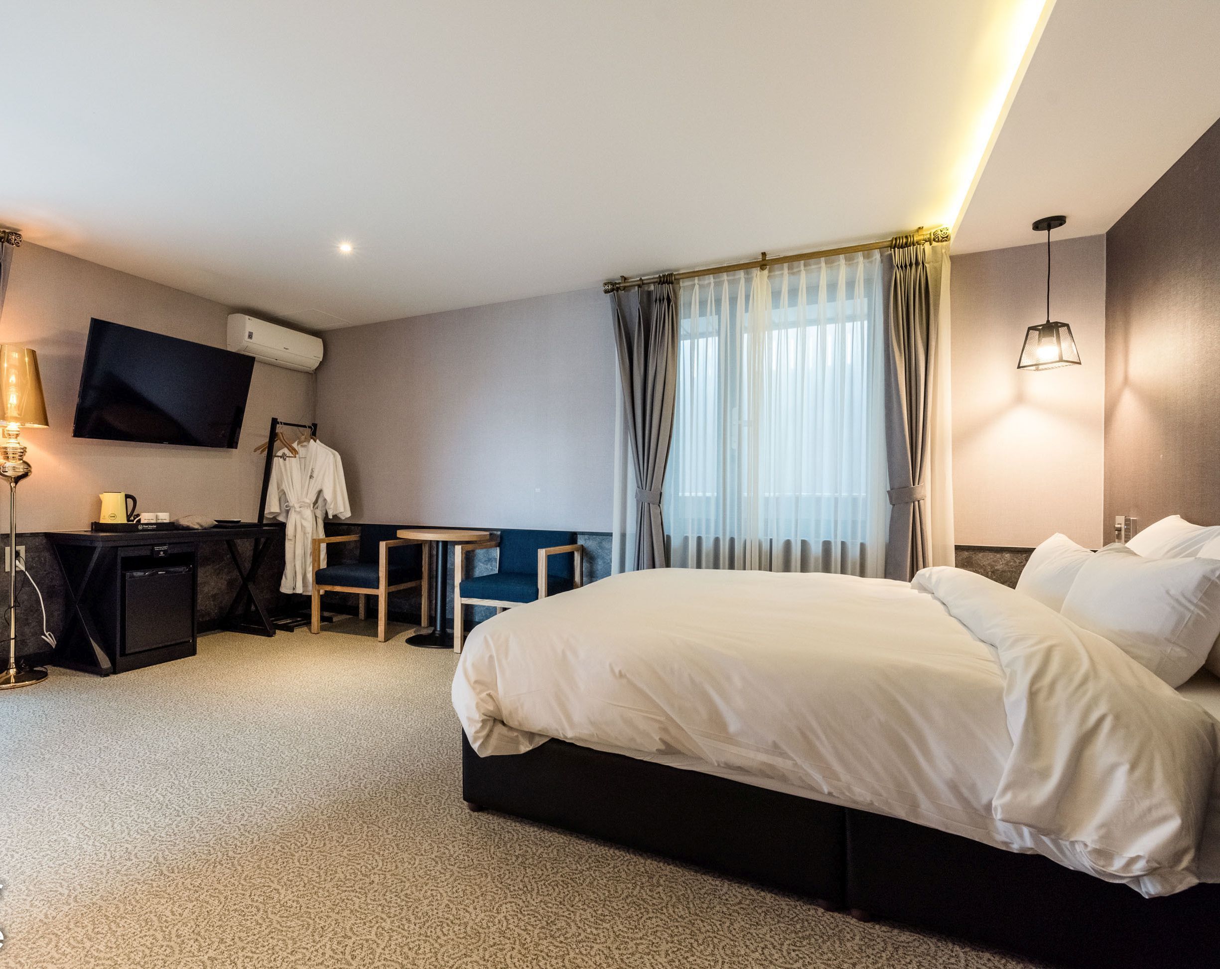 Una habitación de hotel con una cama grande, un escritorio con silla, un televisor y una mesita.
