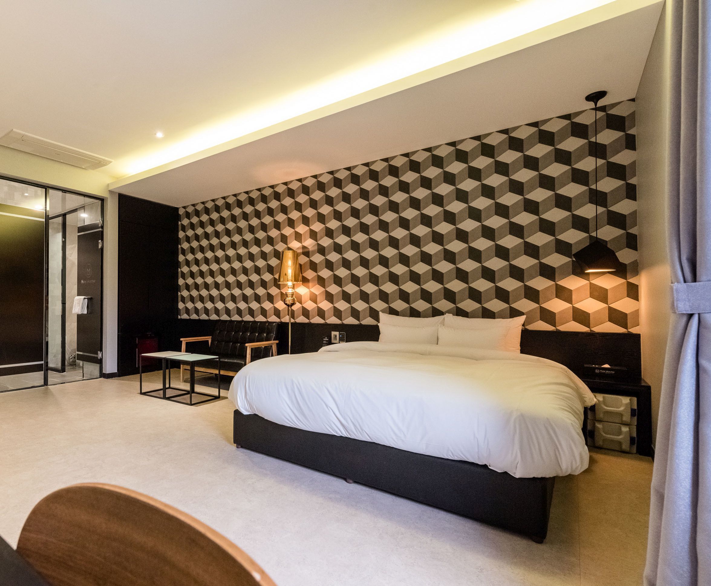Una habitación de hotel moderna con un papel tapiz de diseño geométrico, una cama grande, un escritorio y una silla.