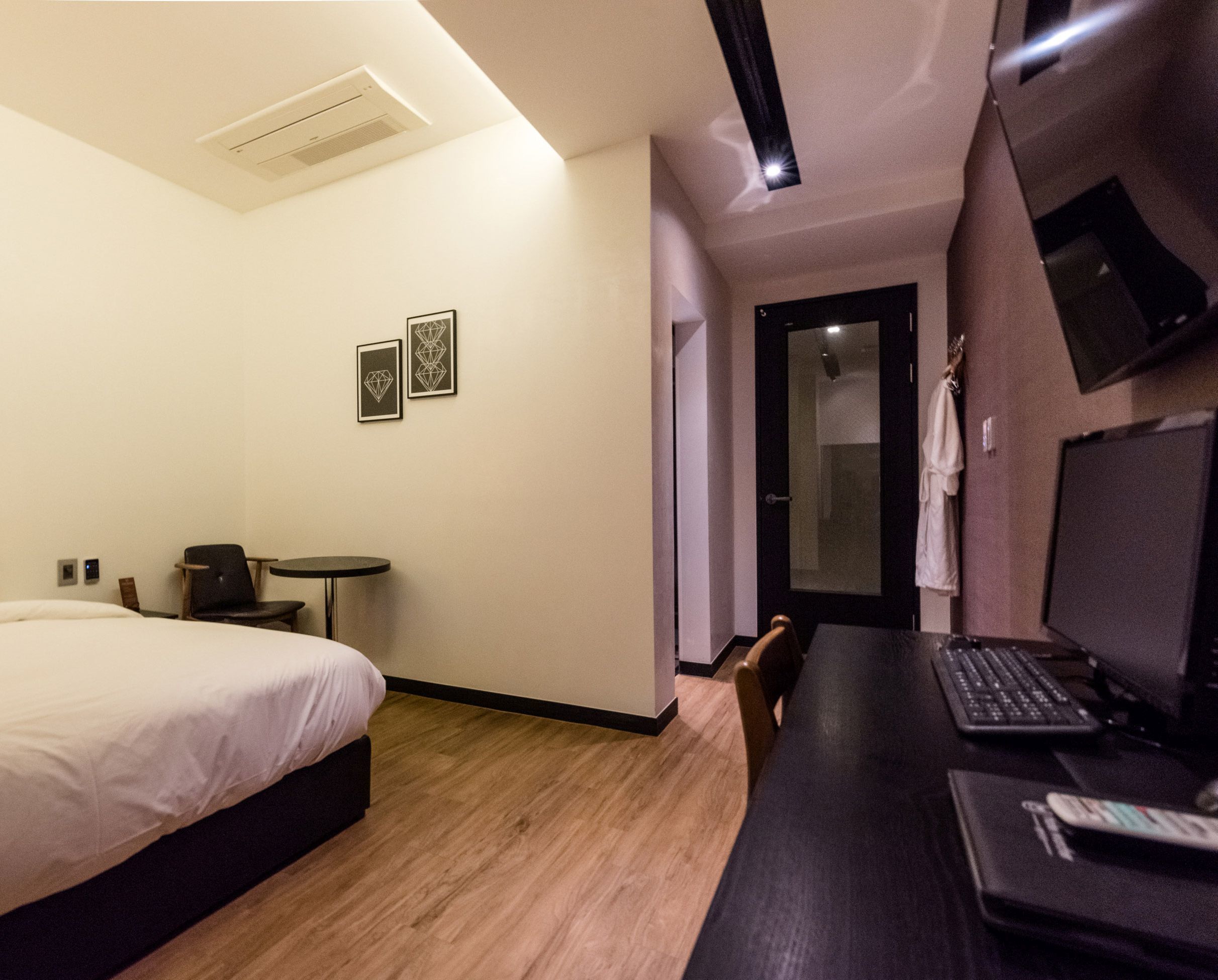 A hotel room with a bed, a desk with a computer, a chair, a small table, and two framed pictures on the wall.
