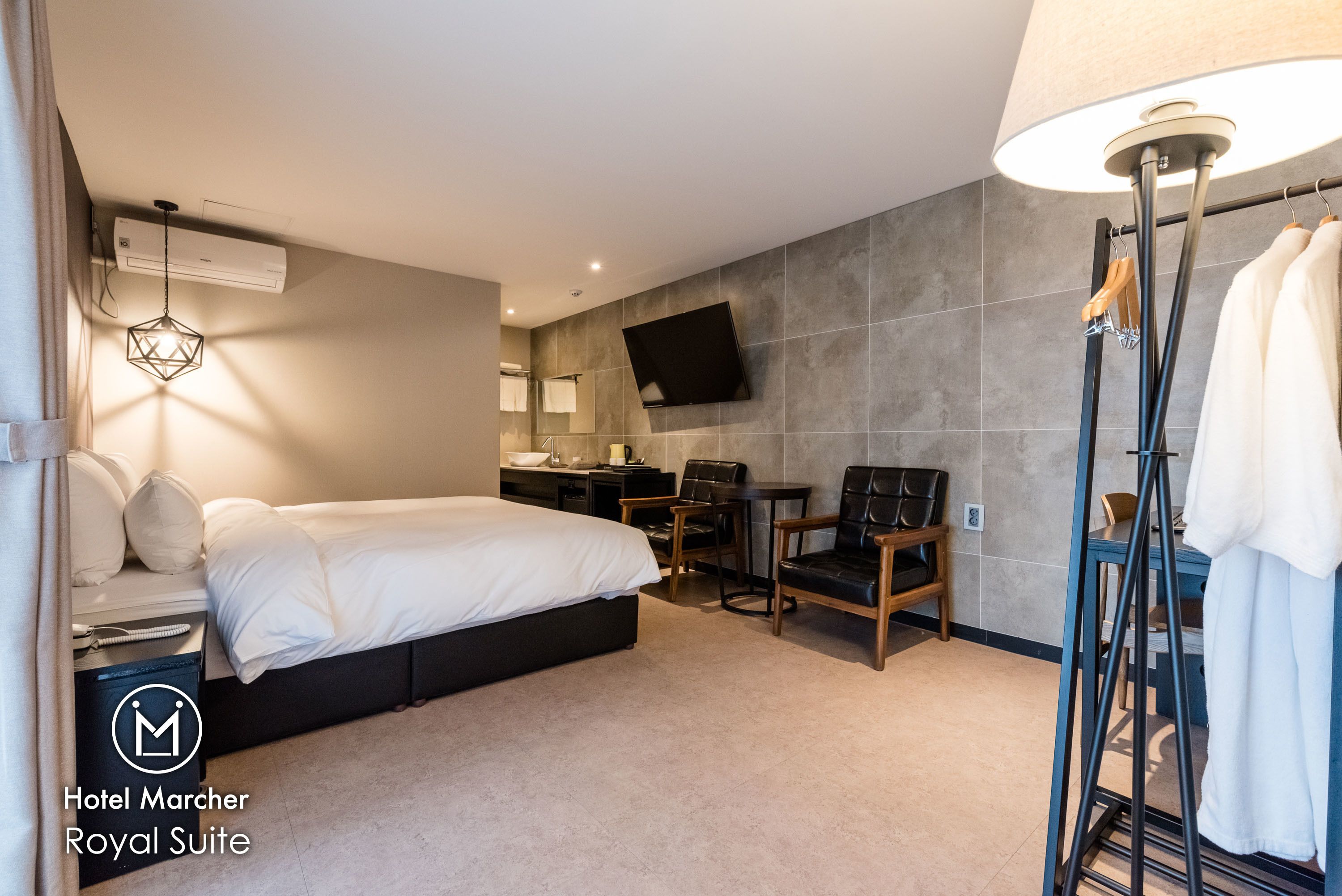 Habitación de hotel con cama, escritorio, silla, televisor montado en la pared y perchero para bata.