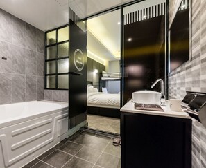 A modern bathroom with a bathtub, a sink, and a mirror. There is a door leading to a bedroom with a bed and a window. - Hotel Marcher (Busan)