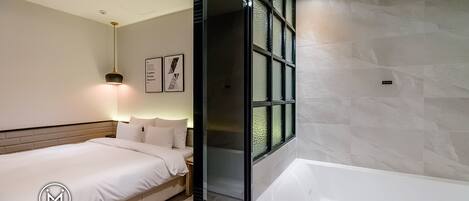 A Deluxe Double room with a bed, bedside table, lamp, and a large window.