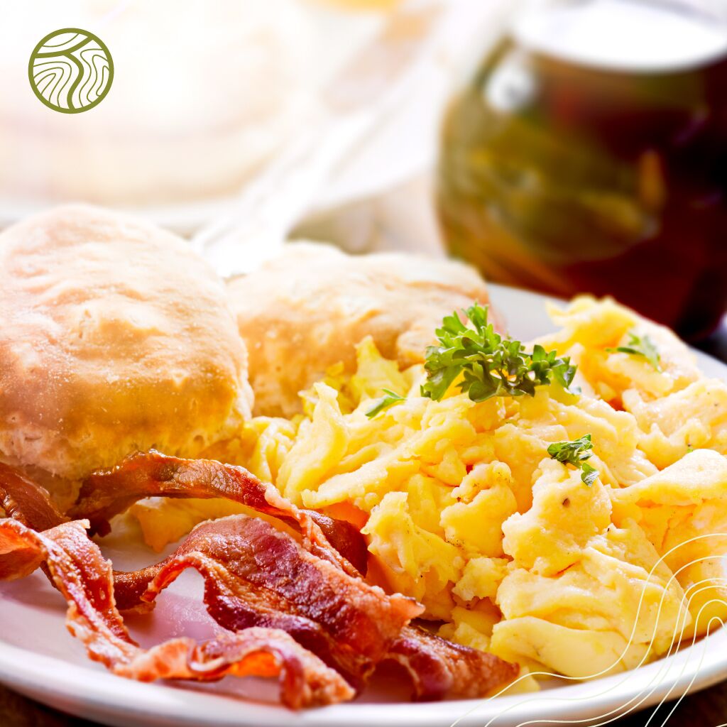 A plate with scrambled eggs, bacon, and a biscuit.