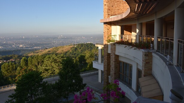 A modern building with a curved balcony overlooking a cityscape and hills. - Timberland Highlands Resort (San Mateo)
