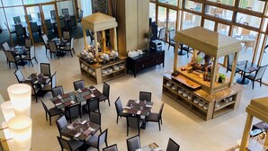 A spacious hotel lobby with multiple dining areas, large windows offering views, and a central decorative fire feature. - Timberland Highlands Resort (San Mateo)